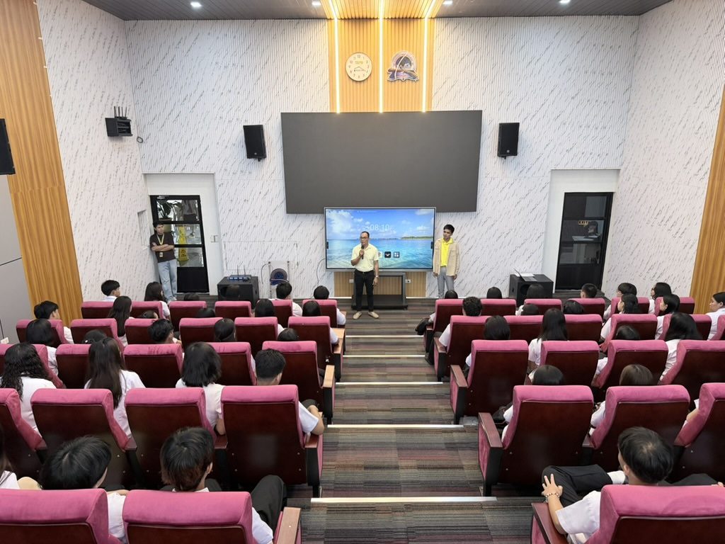 A speaker presenting on stage in Arcinas Hall with the LED wall lit behind them and the audience seated in front.